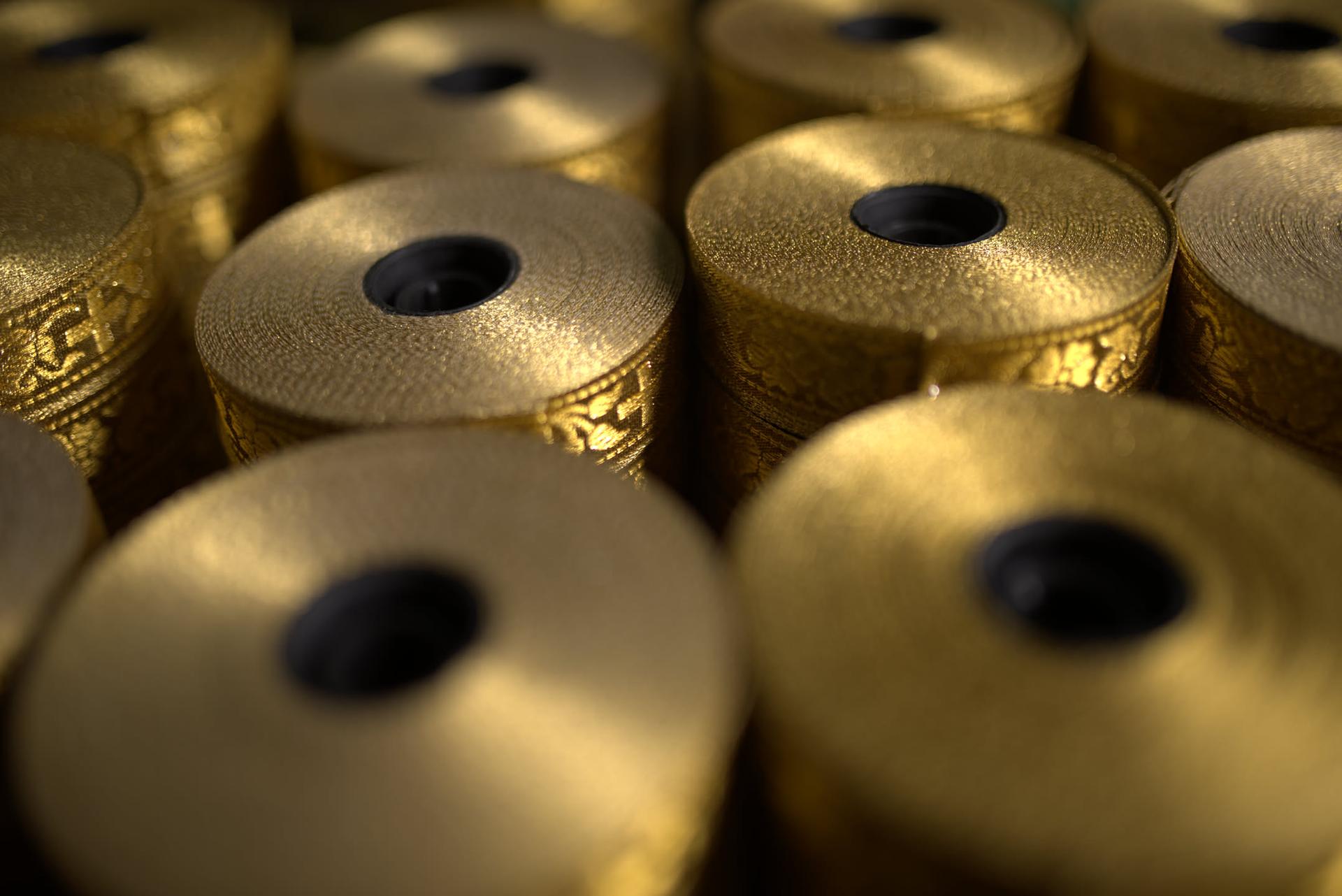Rows of spools wound with gold zari ribbon, stacked close together under a warm mill light.